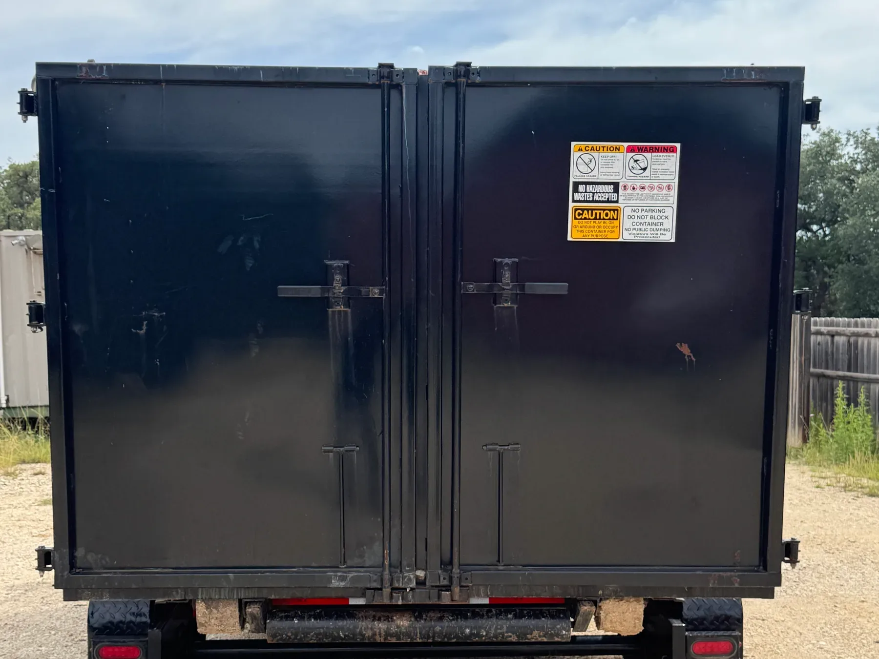 Black commercial dumpster trailer with caution warning labels and rear loading doors