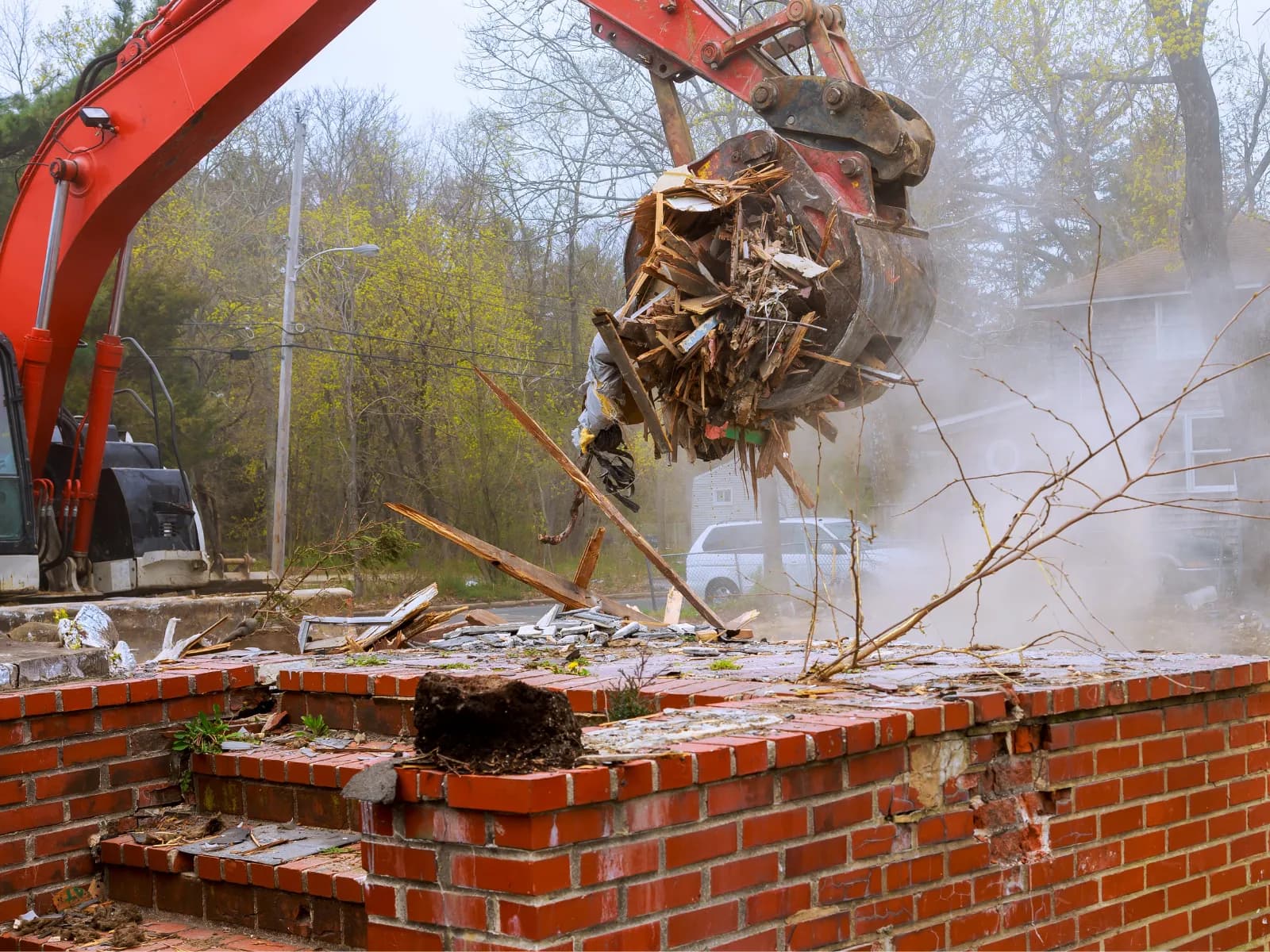 Excavator with grapple attachment removing brick and wood debris from a demolition site