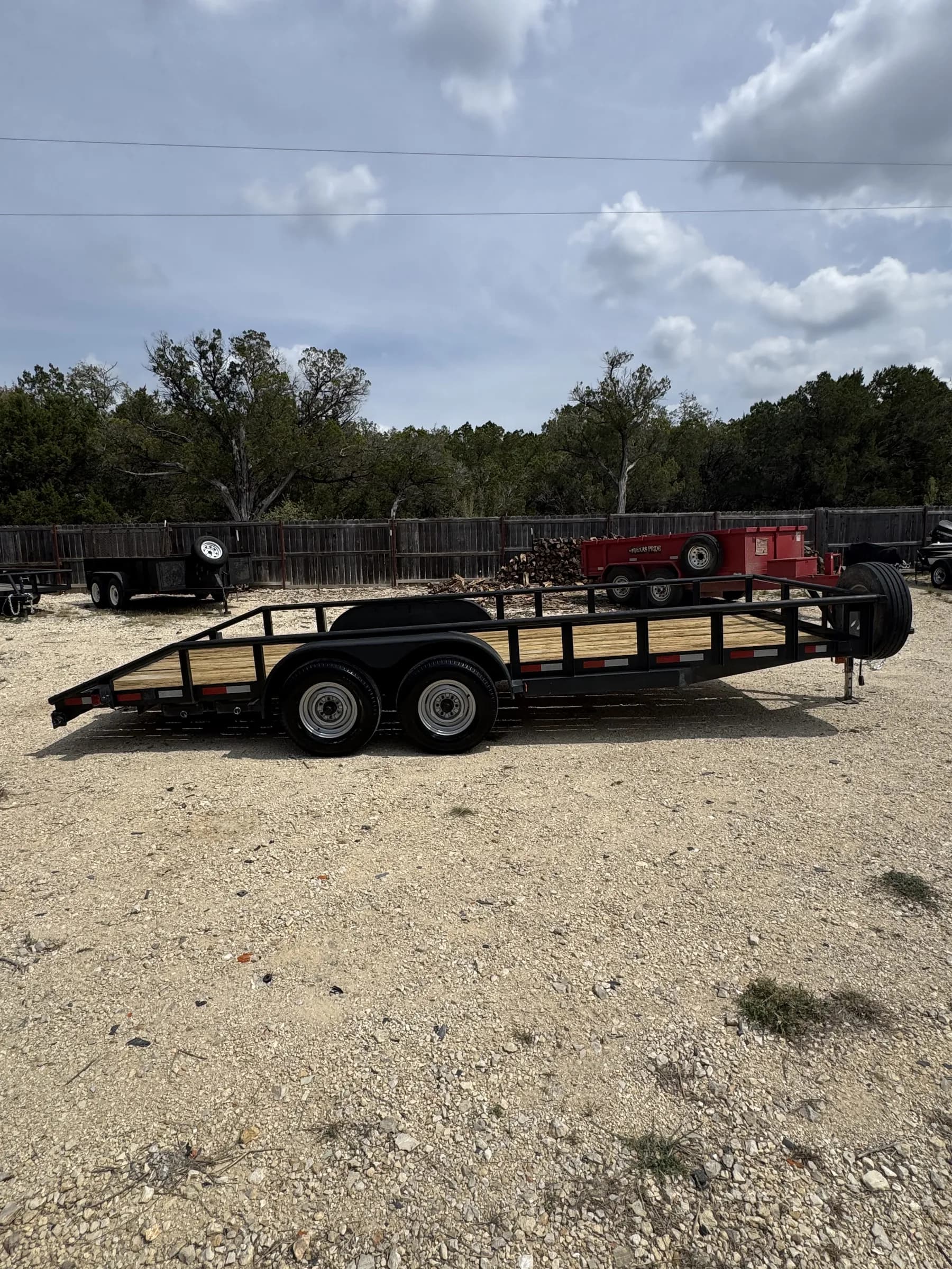 20-foot black tandem axle utility trailer with wood deck and side rails on the RedLine rental lot