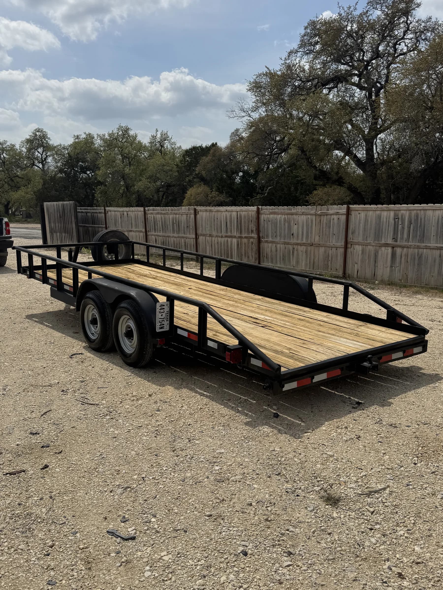 20-foot dual-axle utility trailer with wooden deck and side rails on the gravel rental lot