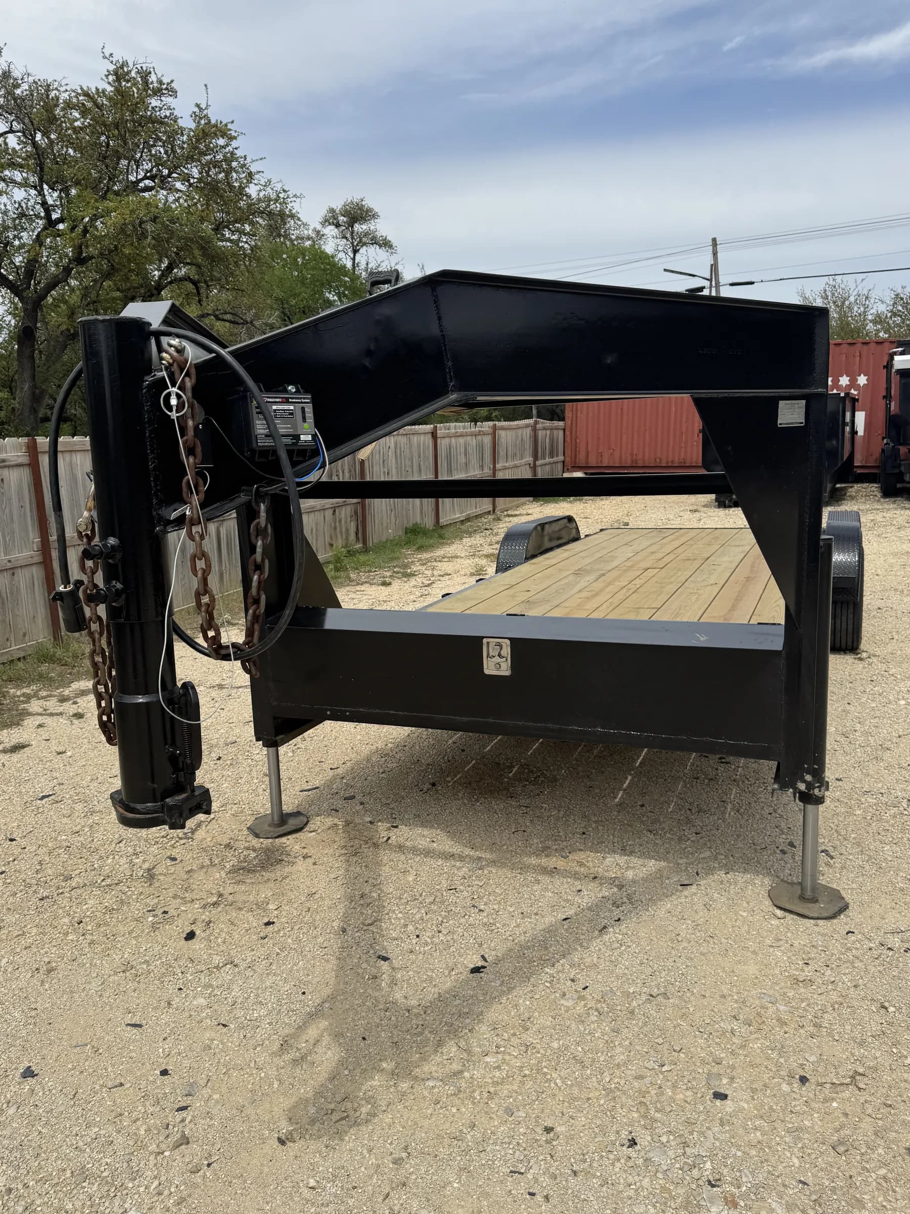 24-foot black gooseneck trailer with wooden deck and stabilizer jacks on the RedLine rental lot