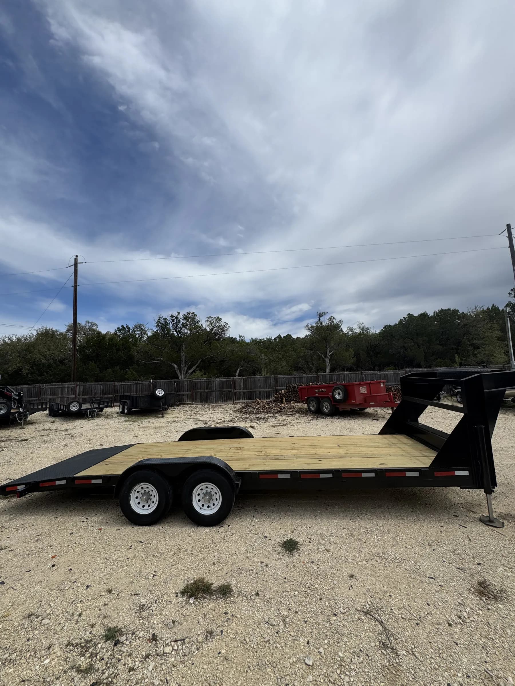 24-foot gooseneck flatbed trailer with wood deck at RedLine rental lot under a dramatic sky
