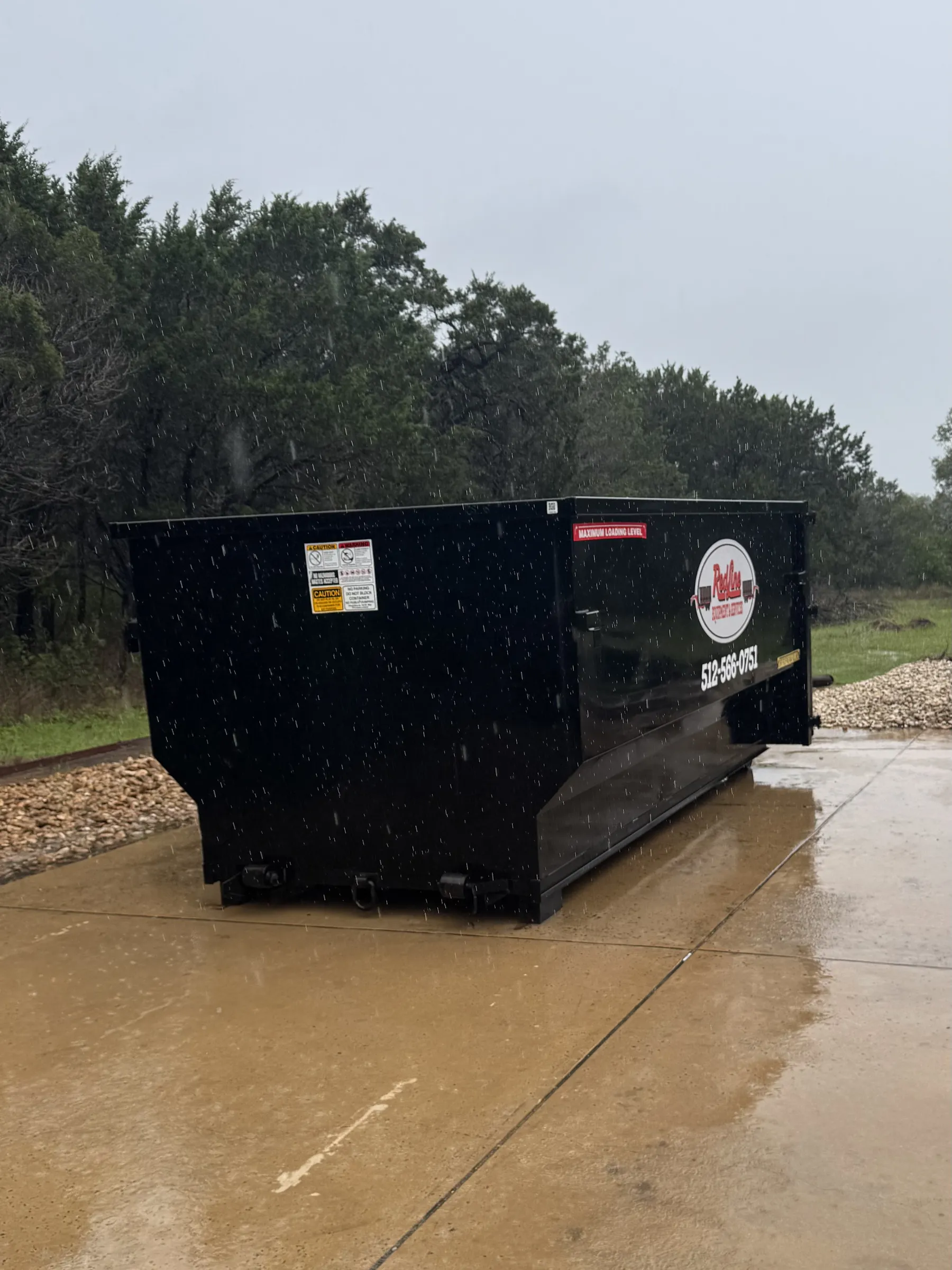 RedLine black roll-off dumpster on a concrete pad in the rain with company logo