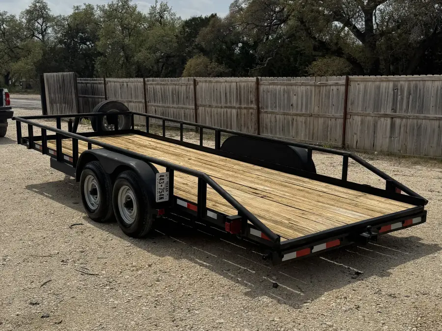 20-foot dual-axle utility trailer with wooden deck and side rails on the gravel rental lot