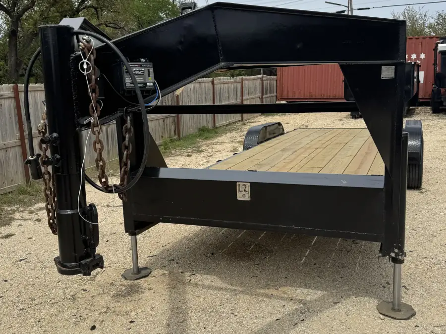 24-foot black gooseneck trailer with wooden deck and stabilizer jacks on the RedLine rental lot