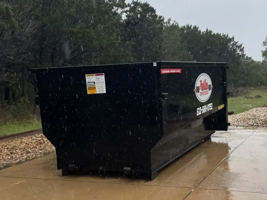 RedLine black roll-off dumpster on a concrete pad in the rain with company logo